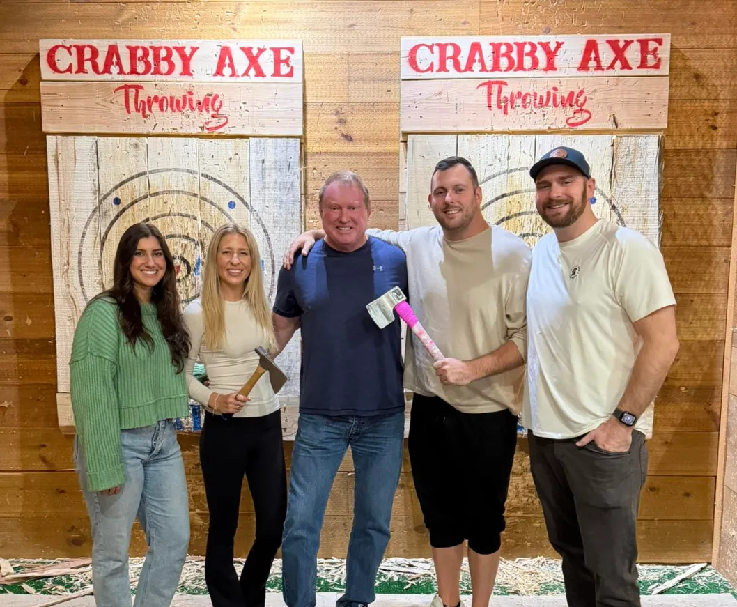 Five people smiling at an axe-throwing venue, standing in front of wooden targets with axes.